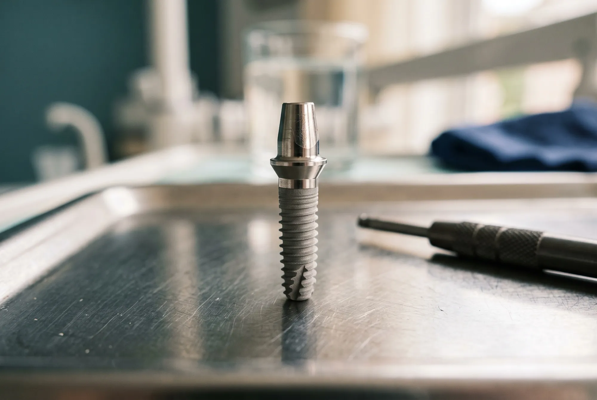 Implant dentar din titan cu bont, așezat vertical pe o tavă de instrumente
